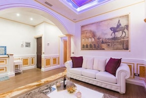 Un salón amplio con un sofá blanco, un cuadro grande de un edificio histórico y suelo de madera.