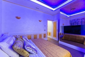 Une chambre à coucher avec un grand lit, une télévision et une porte donnant sur une autre pièce.