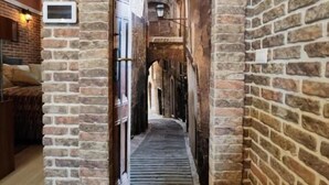Un étroit couloir en briques, doté d’un plancher en bois, mène à une pièce dont un mur est en briques et qui possède une fenêtre.