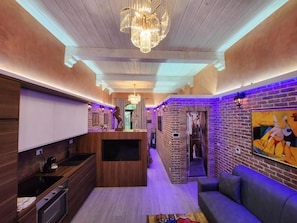 Un intérieur moderne comprenant une cuisine, un coin salon et un couloir aux murs en briques et agrémenté d’un lustre.