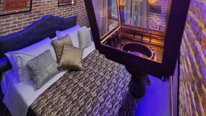 Une pièce avec un lit, un espace clos en verre éclairé par un néon et un mur en briques.