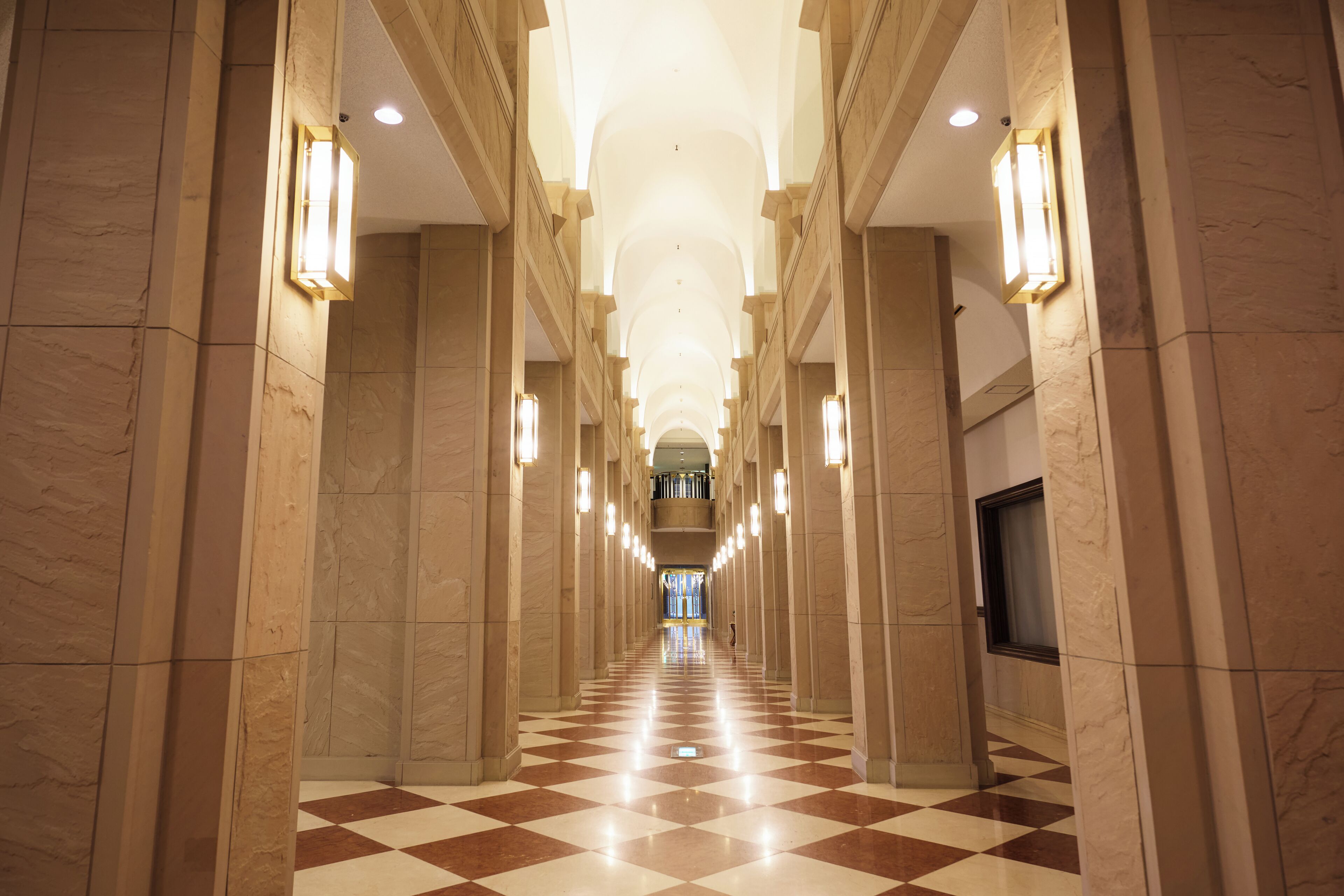 A long, well-lit hallway with checkered flooring and marble walls.