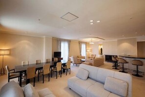 A modern hotel room with a dining area, a sofa, a TV, and a kitchen area.