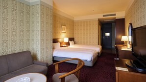 Una habitación de hotel con sofá, dos camas, televisor y escritorio con lámpara.