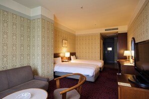 Ett hotellrum med en soffa, två sängar, en tv och ett skrivbord med en lampa.