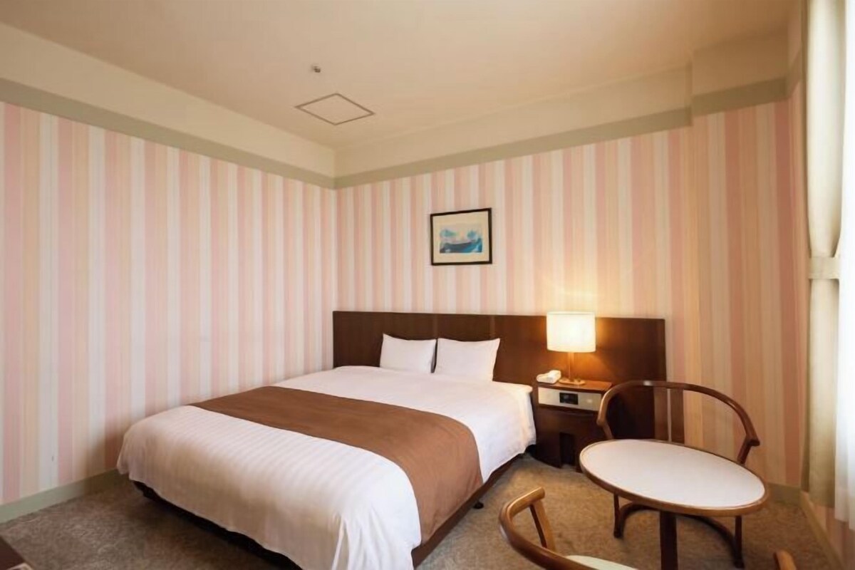 Quarto de hotel com cama, mesa de cabeceira, cadeira e um quadro na parede.