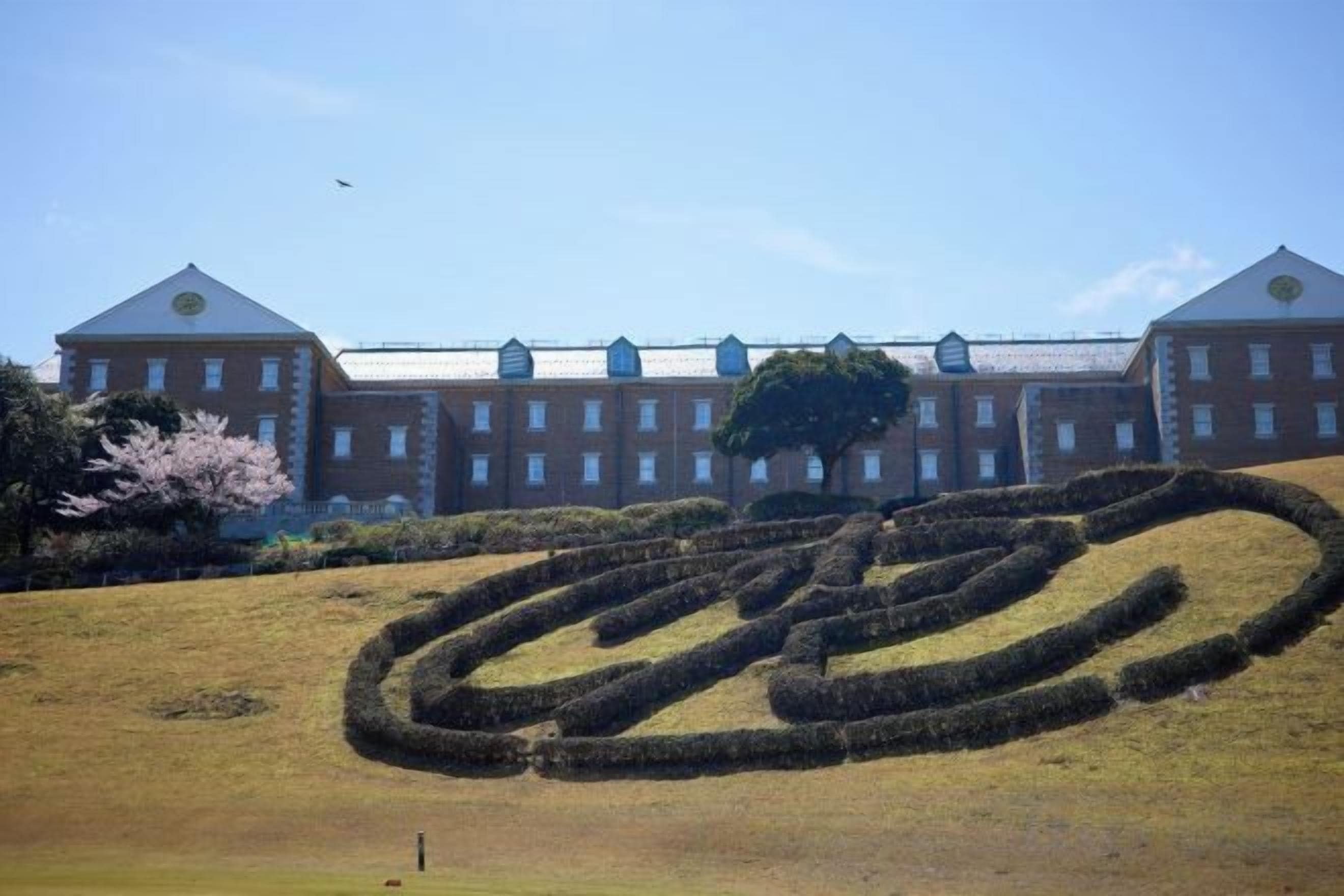 A large building with a symmetrical facade and a circular hedge pattern in the foreground.
