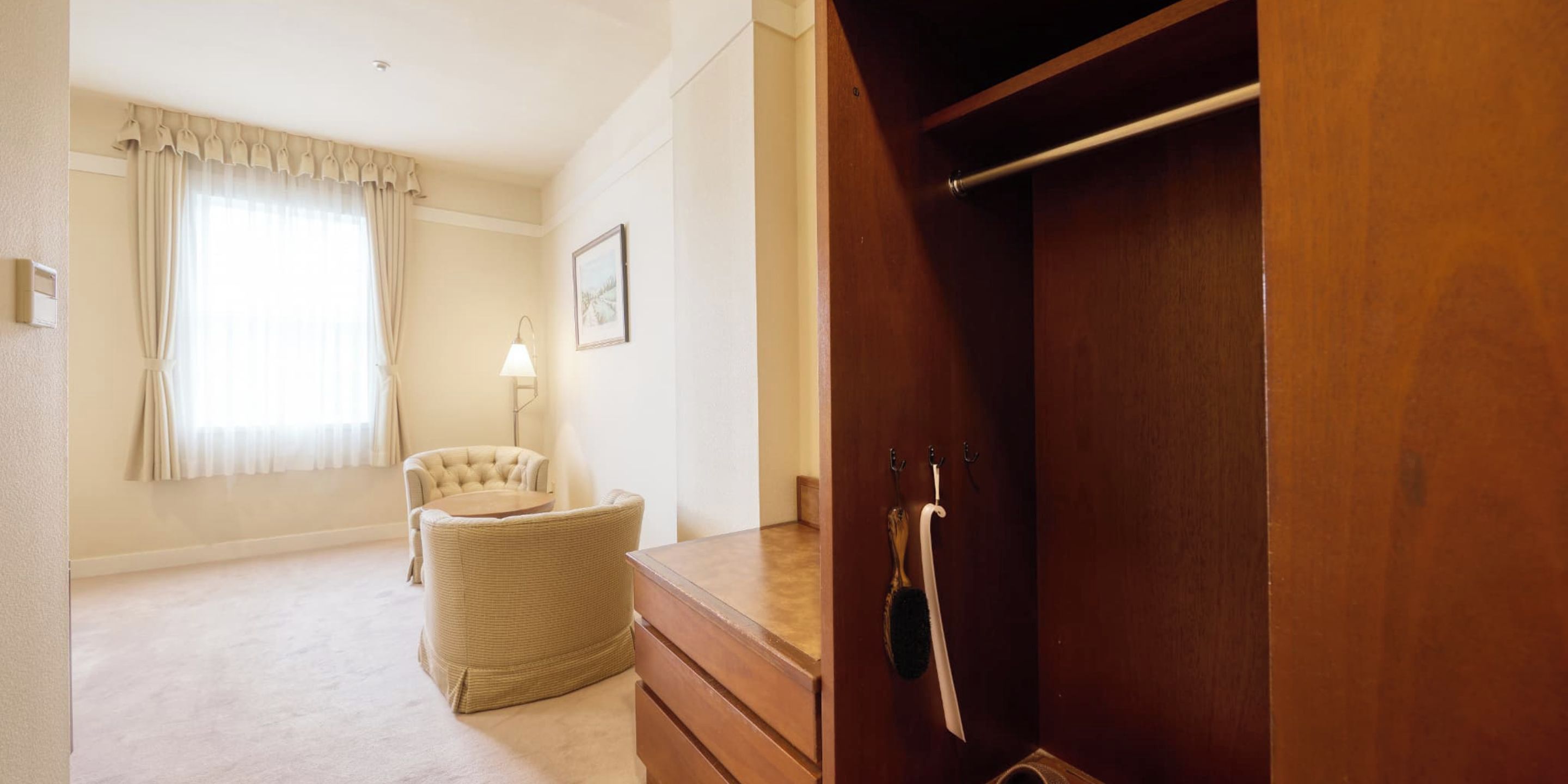 Ein Zimmer mit Holzschrank, Stuhl, Lampe und einem fenster mit Vorhängen.