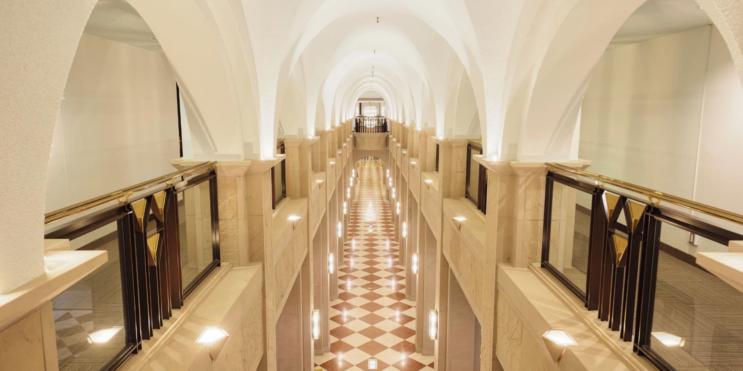 A long, arched corridor with a checkered floor, marble walls, and a central chandelier.