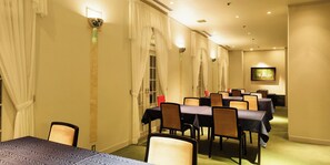 A hotel dining area with multiple tables and chairs, a long corridor, and a painting on the wall.