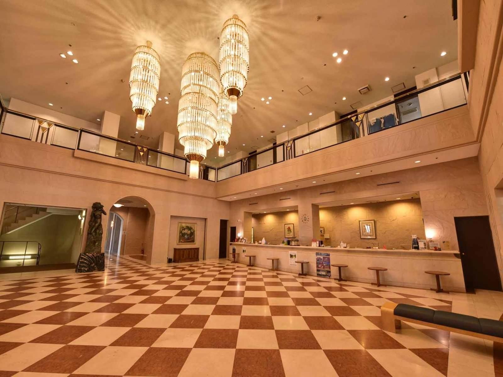 A spacious lobby with a checkered floor, a reception desk, and a staircase leading to an upper level.