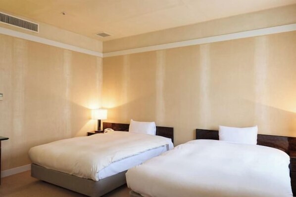 A hotel room with two beds, a nightstand, and a lamp.