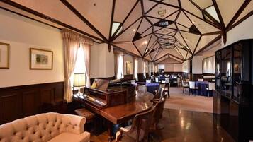 A spacious room with a grand piano, a tufted sofa, and a dining area with chairs and tables.