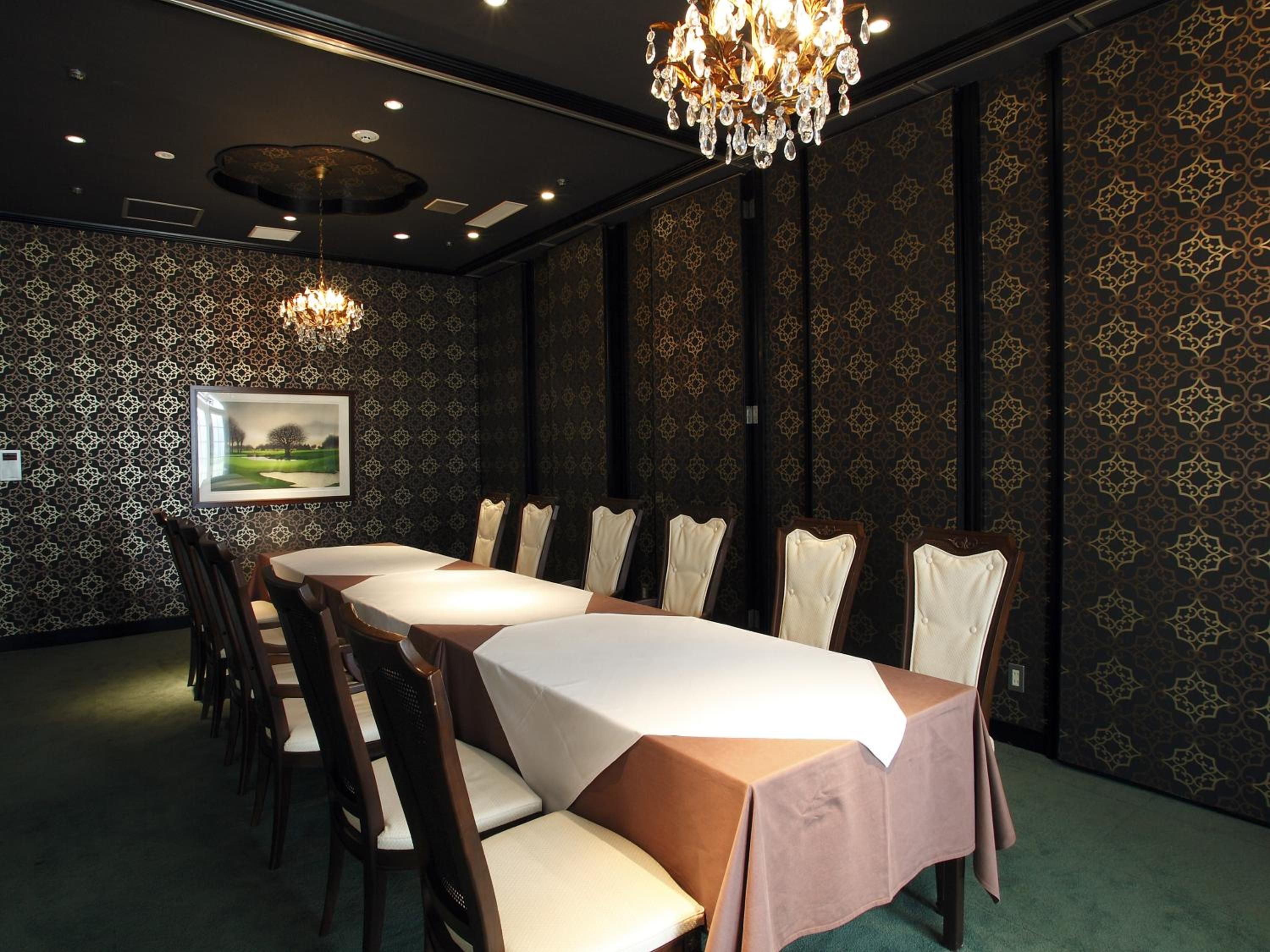 A conference room with a long table, chairs, a chandelier, and patterned wallpaper.