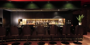 A bar area with a long counter, multiple stools, and a variety of bottles.