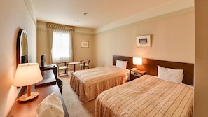 A hotel room with two beds, a desk with a lamp, a chair, a small table, and a window with curtains. - Yugashima Golf Club & Hotel Resort (Izu)
