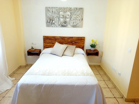 A bedroom with a wooden headboard, a bed with white bedding, two bedside tables with lamps, and a wall-mounted artwork.. Charming House in Vejer de la Frontera, Cádiz