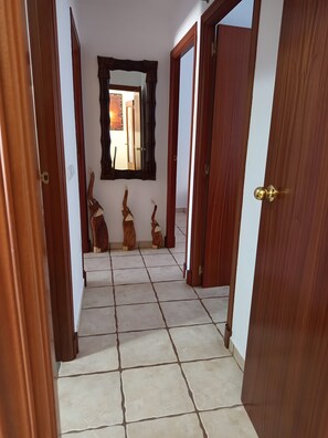 Un corridoio con pavimento piastrellato, porte in legno e uno specchio appeso al muro.