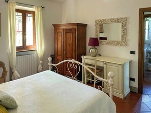 Ein Schlafzimmer mit einem Bett, einem Holzschrank, einem Schminktisch mit Spiegel und einem Fenster mit Vorhängen.