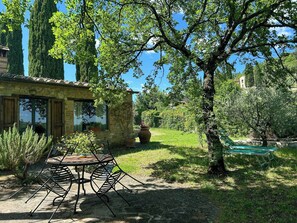 Ein Steinhaus mit Terrasse, Sitzgelegenheiten im Freien und einem Garten mit Bäumen und Pflanzen.