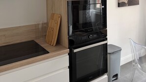 Cozinha moderna com forno embutido, micro-ondas e tábua de corte de madeira no balcão.