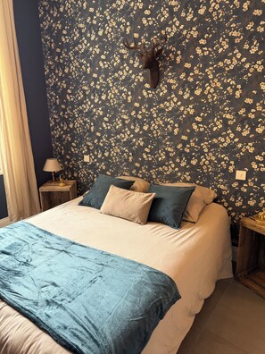 Un lit avec un papier peint à motifs floraux, une tête de cerf accrochée au mur et une table de chevet avec une lampe.