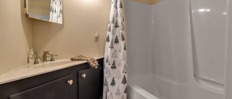 Un baño con bañera, espejo, lavamanos con grifos y cortina de ducha con estampado de árboles.