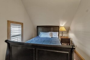 Ein Schlafzimmer mit einem Bett, einem Nachttisch, einer Lampe, einem Fenster mit Jalousien und einem Holz-Kopfteil.