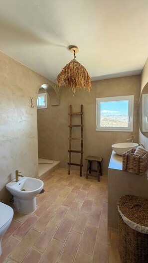 Ein Badezimmer mit einer Bidet-Funktion, einer Holzleiter, einem Fenster mit Aussicht und einem gewebten Korb.