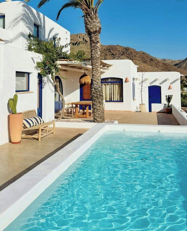 Ein Poolbereich mit blauem Wasser, weißen Gebäuden und einer Palme.