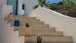 A set of concrete stairs leading up to a white building with a blue door, surrounded by greenery and a clear sky. - Mediterranean-style house in Cabo de Gata (Almeria)