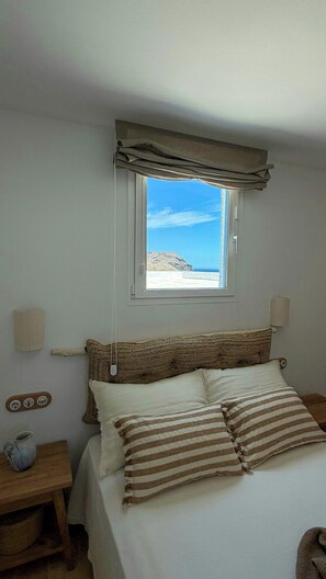 Ein Schlafzimmer mit einem Bett, einem Fenster mit Meerblick, einer Nachttischlampe und einem Holznachttisch.