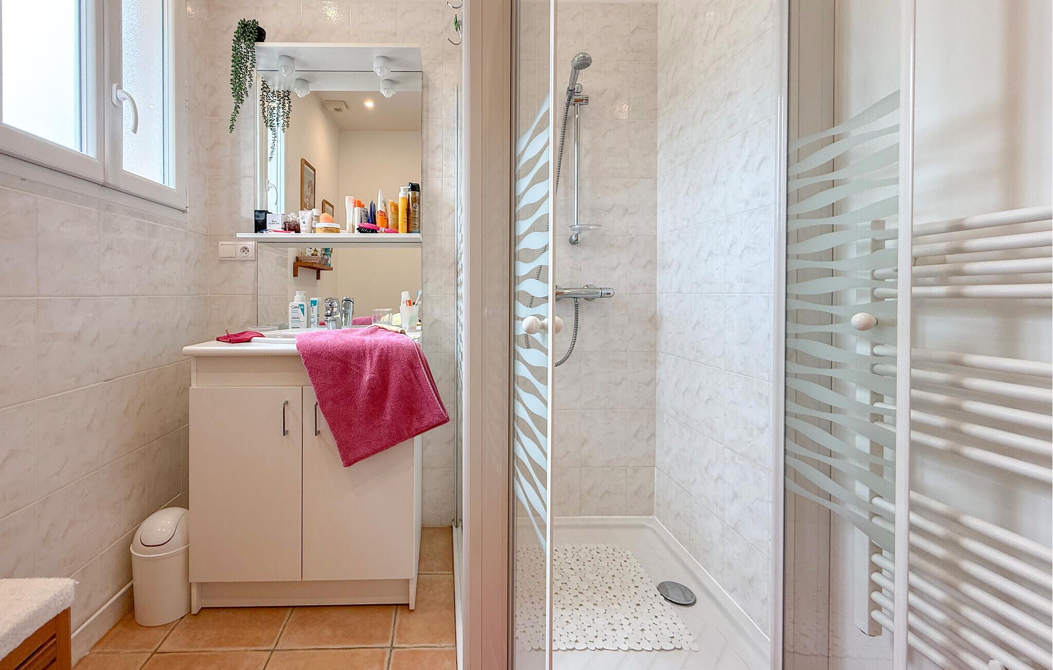 A bathroom with a shower, a sink with toiletries, a mirror, and a towel rack.