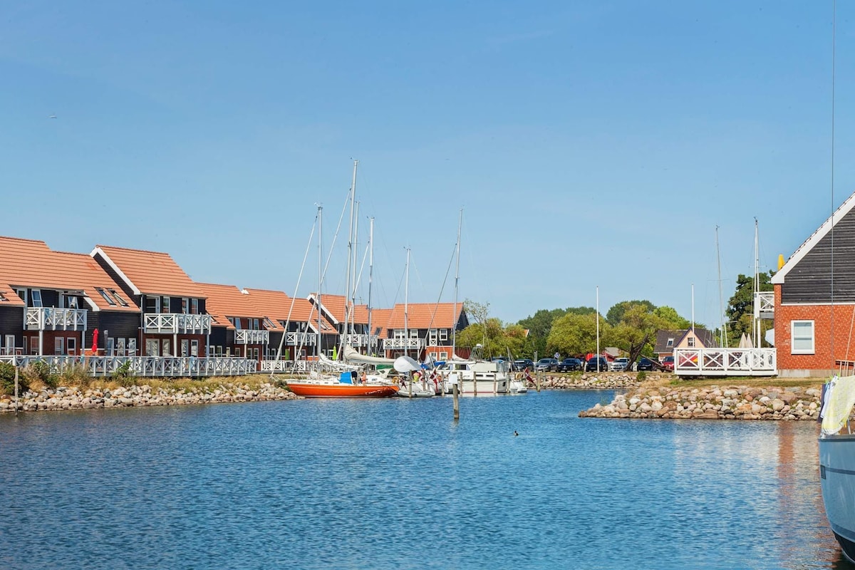 A marina with boats docked, a small island with a gazebo, and buildings with red roofs.