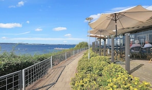 A waterfront restaurant with outdoor seating, a view of the sea, and a pathway along the water. - Faaborg Holiday Center (Faaborg)