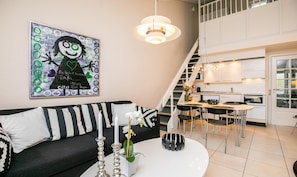 A modern living room with a black and white sofa, a white coffee table, and a staircase leading to a kitchen.