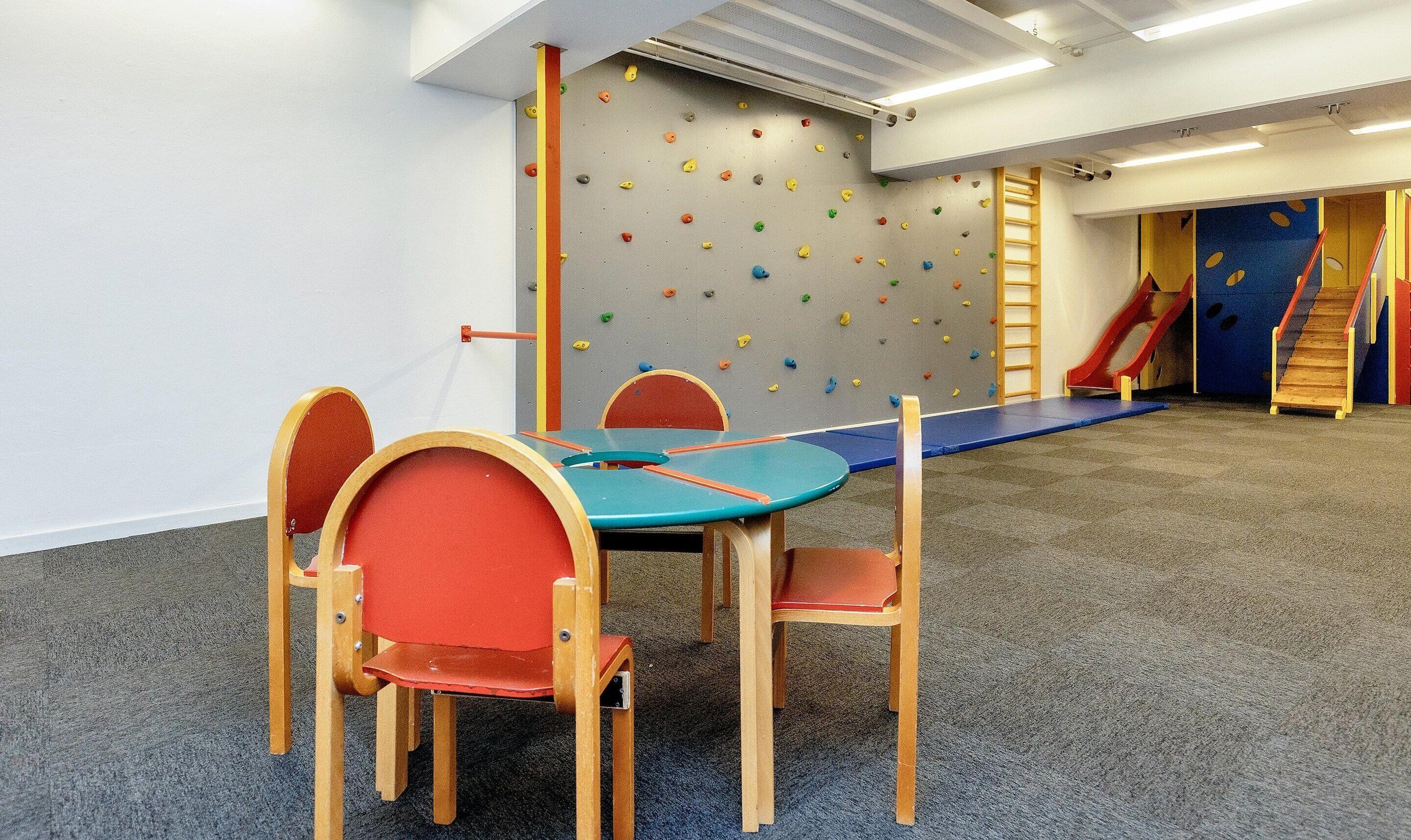 Ein Spielzimmer mit Kletterwand, Rutsche und Tisch mit Stühlen.