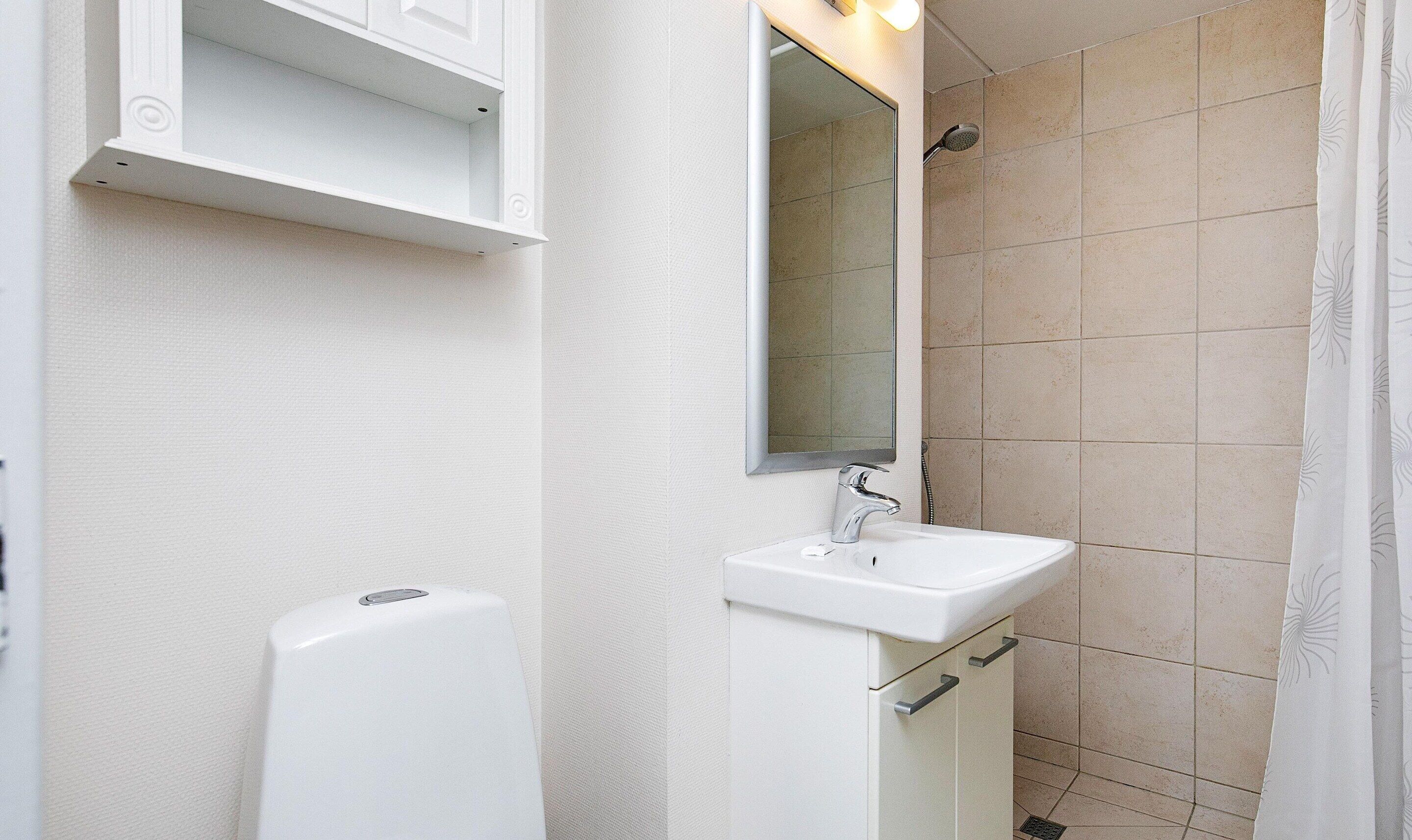 Un baño con lavamanos blanco, espejo y ducha.
