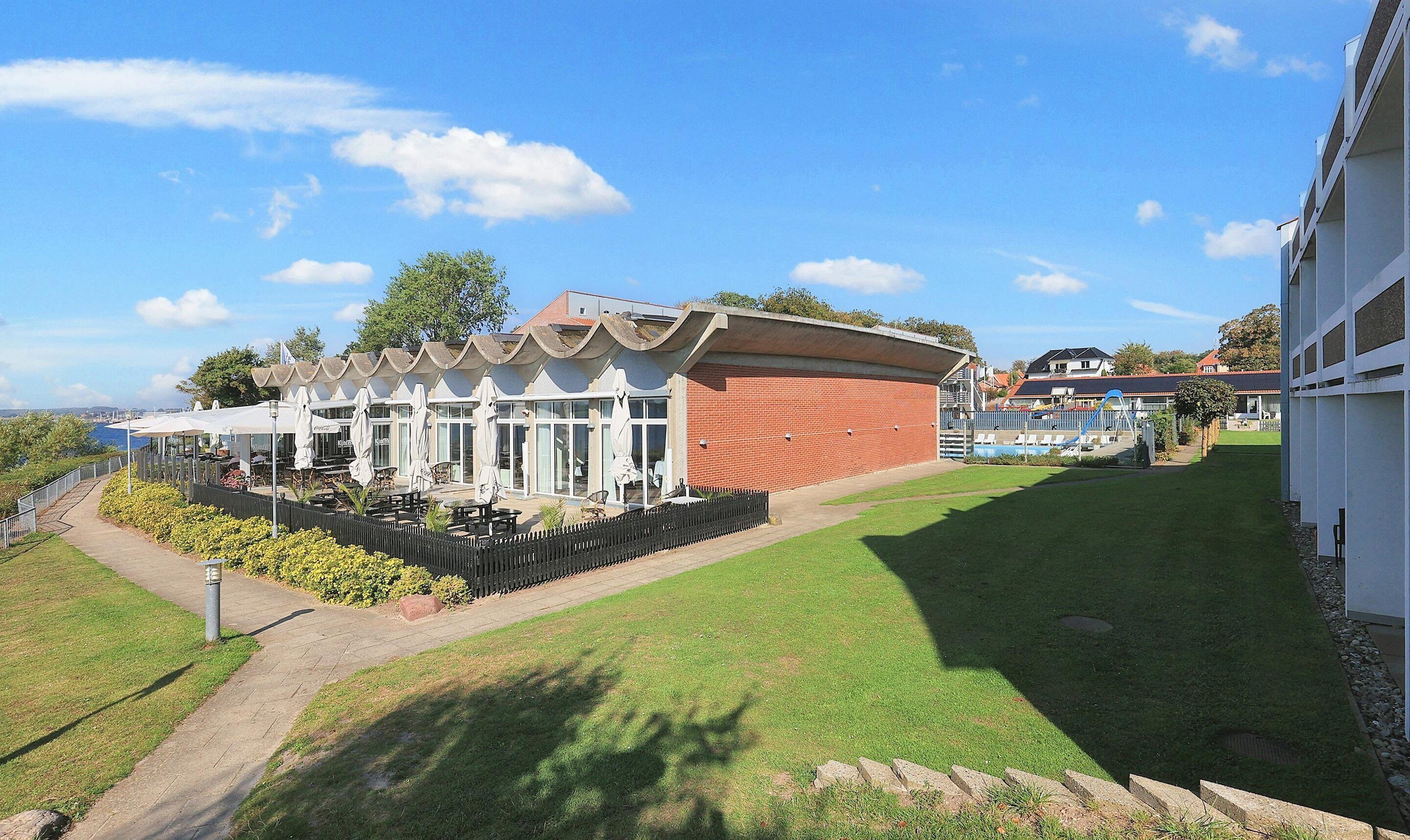 A building with a brick facade, a covered outdoor seating area with umbrellas, and a view of the sea.