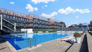 Una piscina con superficie de agua azul cristalina, rodeada de sillas de descanso y un edificio con varios balcones.