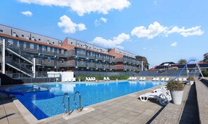 A swimming pool with a clear blue water surface, surrounded by lounge chairs and a building with multiple balconies. - Faaborg Holiday Center (Faaborg)
