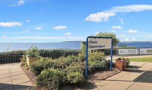 A sign indicating a sauna and swimming pool, with a view of the sea and a fence with greenery. - Faaborg Holiday Center (Faaborg)