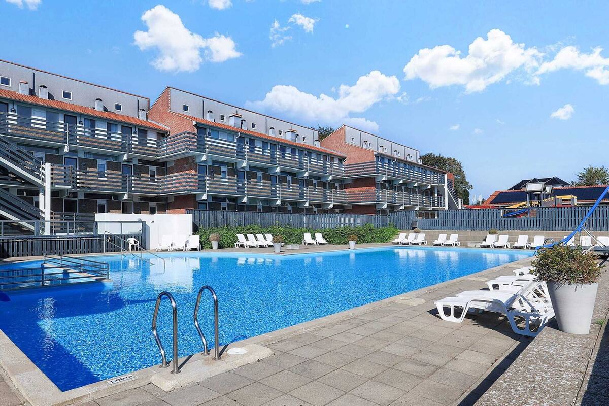 A swimming pool with lounge chairs and a building with multiple balconies in the background.