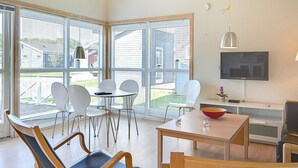 Una sala de estar moderna con ventanas amplias, un televisor de pantalla plana y un comedor con sillas y una mesa.