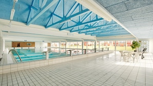 An indoor swimming pool with a tiled floor, a diving board, and a covered area with seating. - Lemvig Coastal Stay (Lemvig)