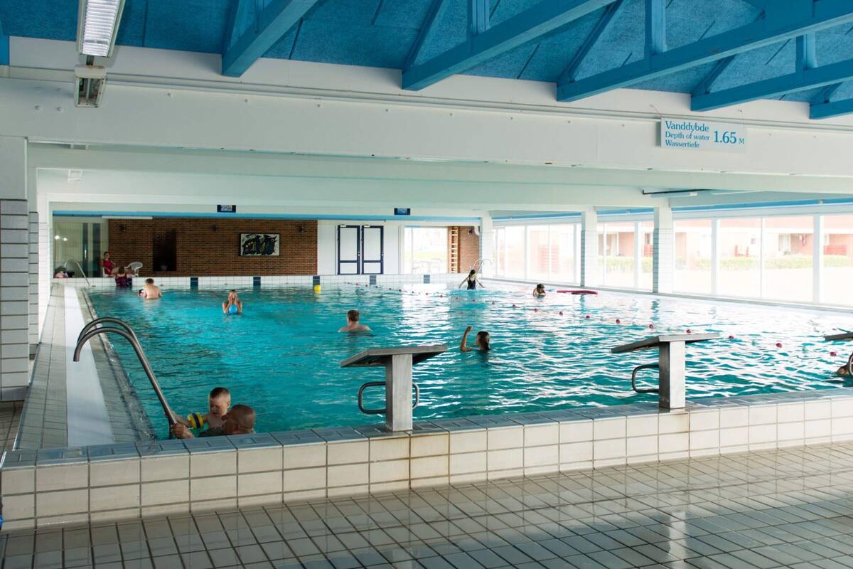 Una piscina interior con varias pistas de natación, suelo de baldosas y techo alto con vigas azules.
