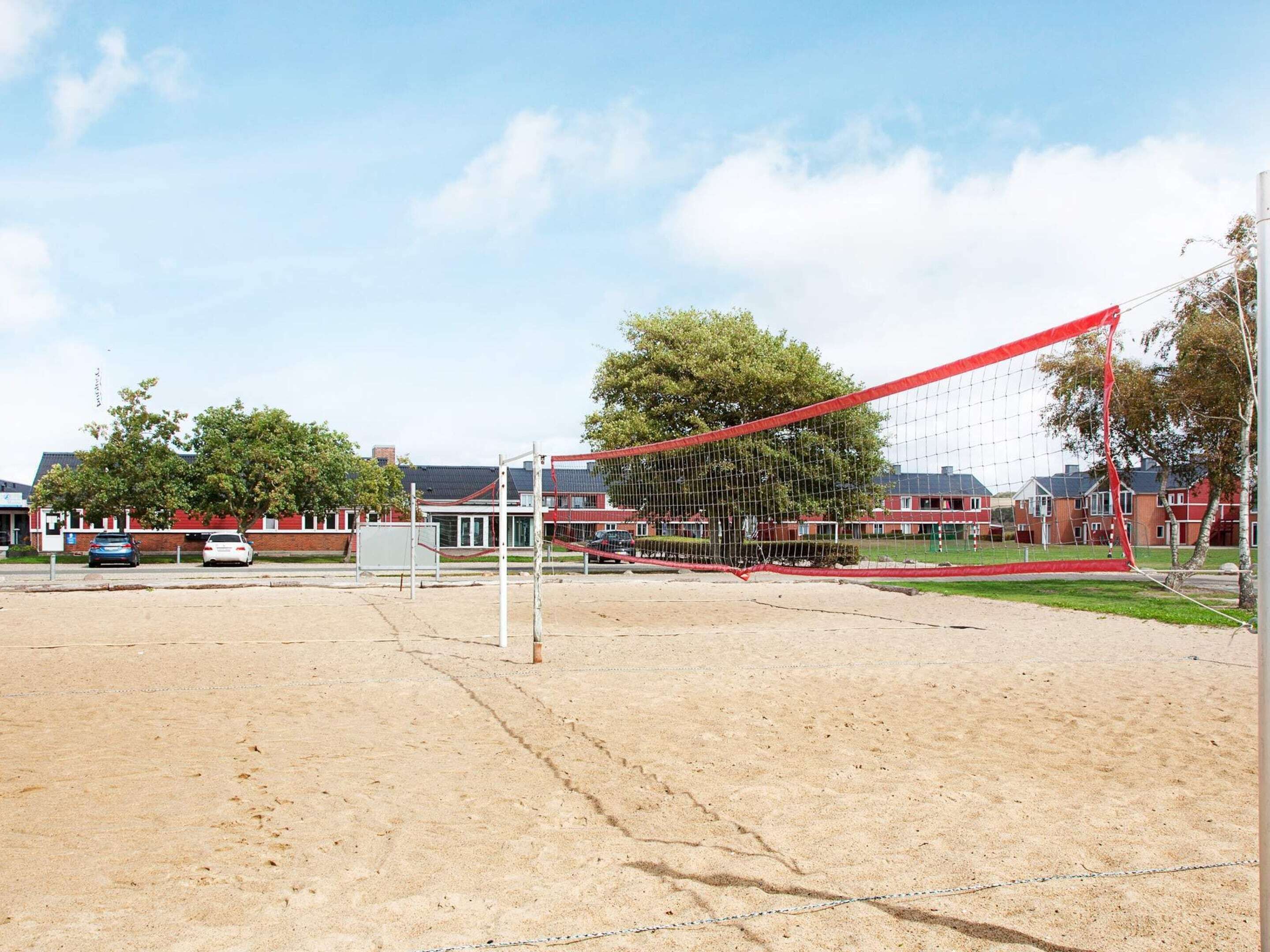 A sandy sports field with a volleyball net, surrounded by buildings and trees.