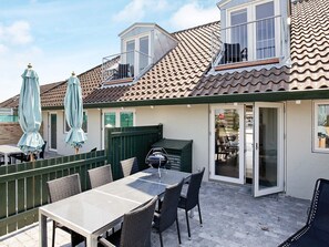 Eine Terrasse mit Tisch, Stühlen, einem Grill und Sonnenschirmen.