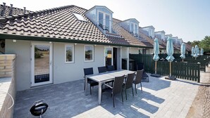 A patio with a table and chairs, a grill, and a fenced area with umbrellas. - Karrebaeksminde Apartments (Karrebæksminde)
