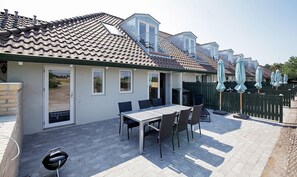 Eine Terrasse mit Tisch und Stühlen, einem Grill und einem umzäunten Bereich mit Sonnenschirmen.